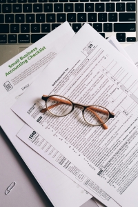 A pair of glasses sits on top of a stack of accounting documents next to a laptop keyboard.